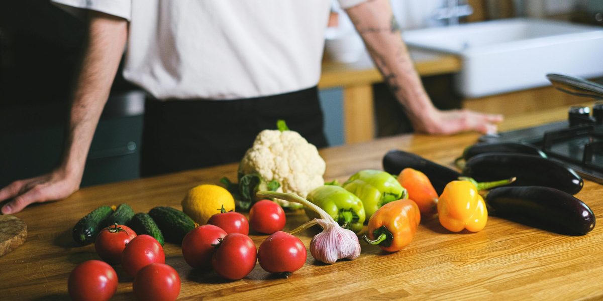 Diverse fresh vegetables on kitchen countertop with a person in the background. Perfect for healthy lifestyle content.