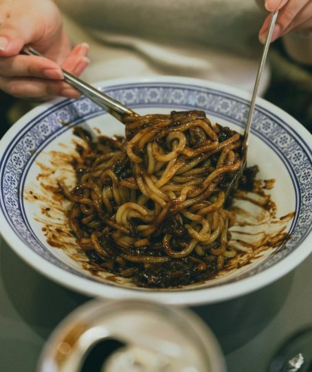 Close-up of a person enjoying traditional Korean jajangmyeon with chopsticks, highlighting Korean cuisine.