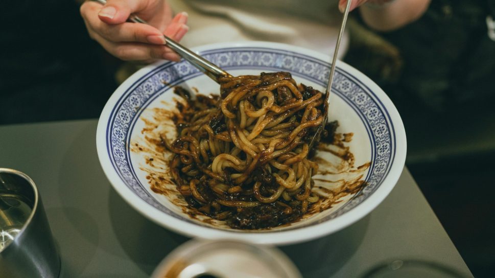 Close-up of a person enjoying traditional Korean jajangmyeon with chopsticks, highlighting Korean cuisine.