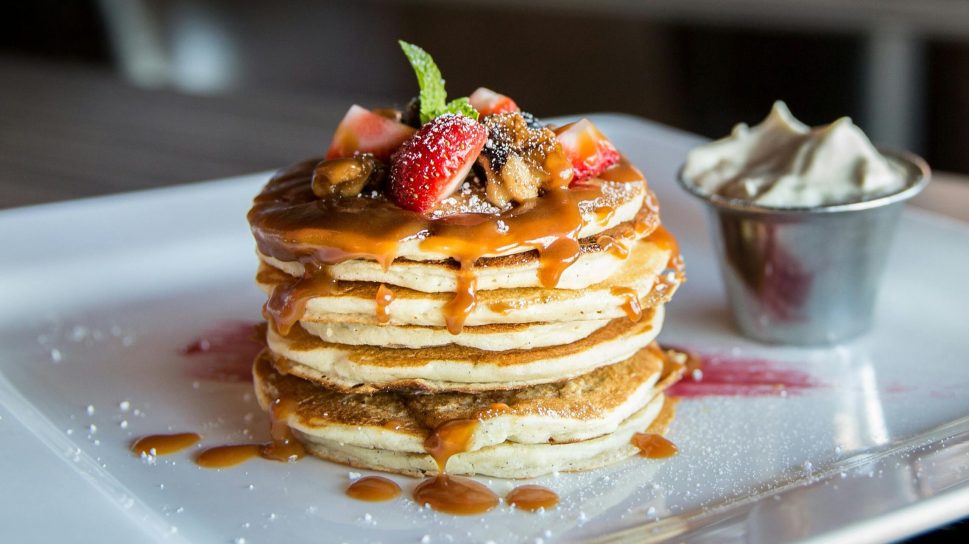 Mouthwatering pancakes with strawberries, nuts, and syrup on a plate.