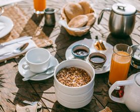 An inviting breakfast setup with granola, tea, juice, and fresh bread on a rustic table.
