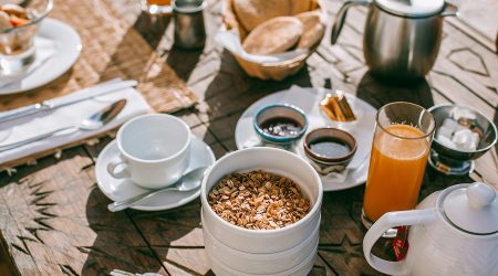 An inviting breakfast setup with granola, tea, juice, and fresh bread on a rustic table.