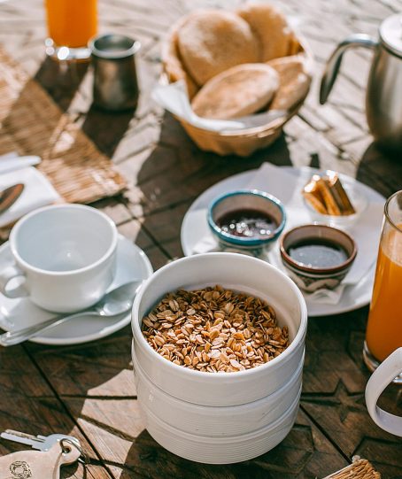 An inviting breakfast setup with granola, tea, juice, and fresh bread on a rustic table.