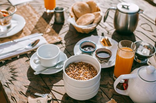 An inviting breakfast setup with granola, tea, juice, and fresh bread on a rustic table.