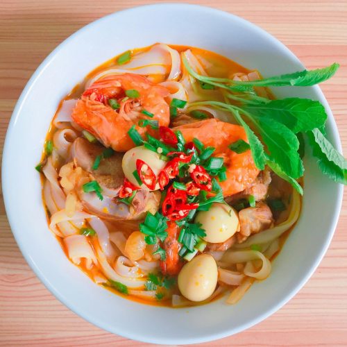 A vibrant bowl of Vietnamese noodle soup with shrimp, herbs, and quail eggs.