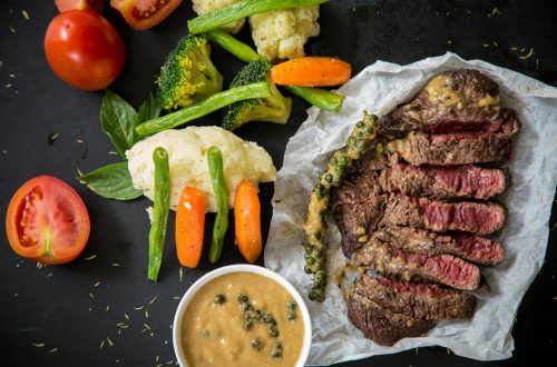Grilled steak served with fresh vegetables and pepper sauce, presenting a colorful and appetizing meal.