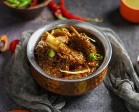 Close-up of a spicy mutton curry served in a traditional copper bowl, showcasing rich Indian flavors.