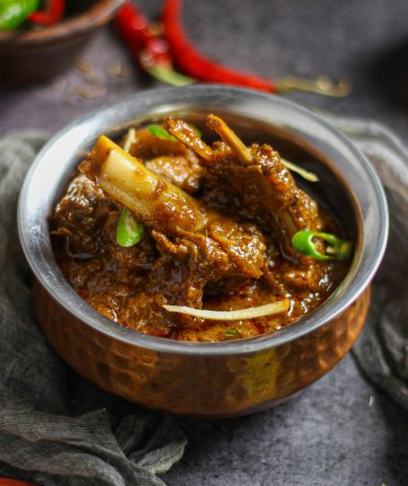 Close-up of a spicy mutton curry served in a traditional copper bowl, showcasing rich Indian flavors.